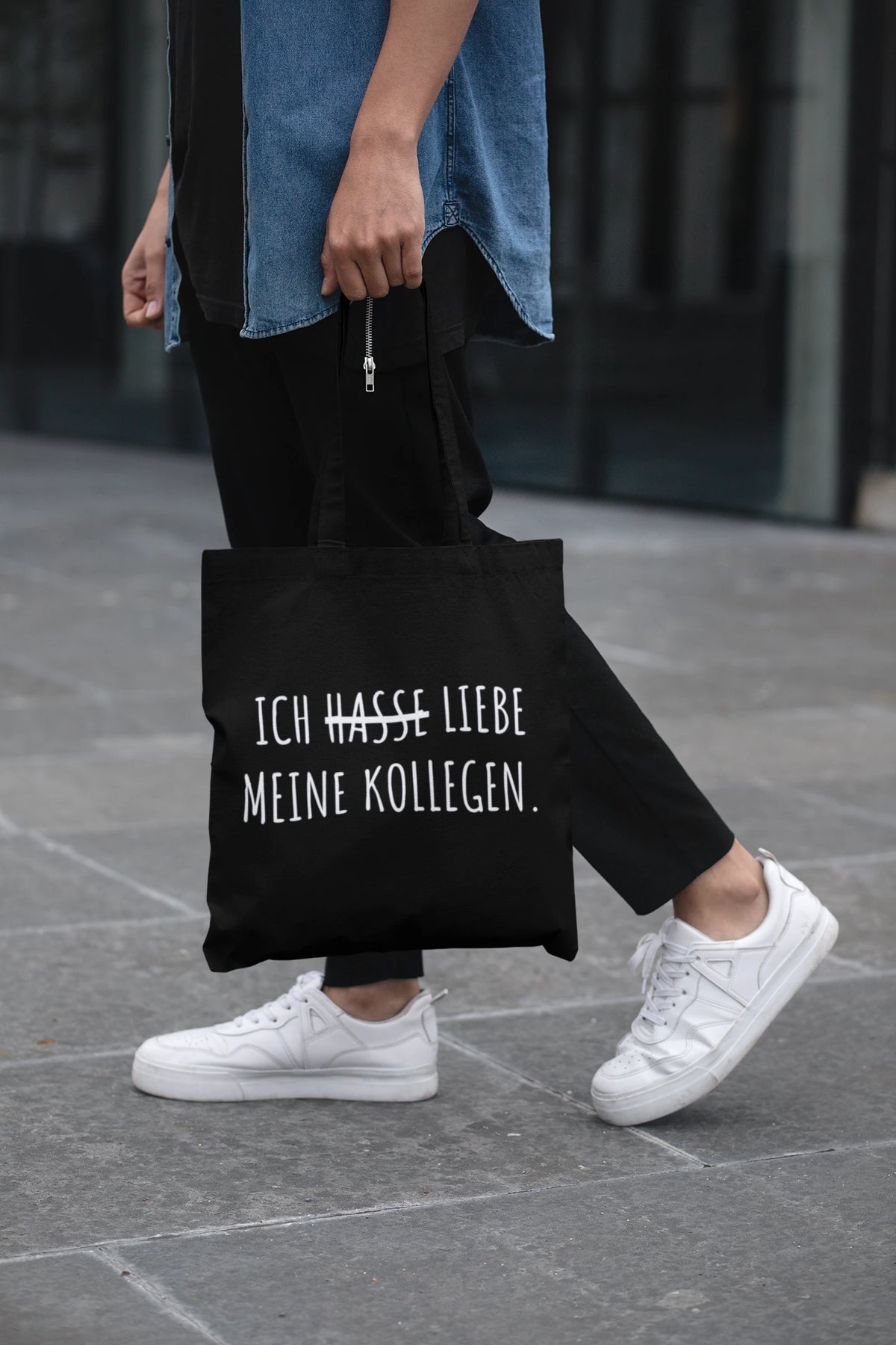 Schwarze Tragetasche mit Spruch "Ich liebe meine Kollegen" (durchgestrichenes "Hasse") von Vollzeitfrust, getragen auf der Straße