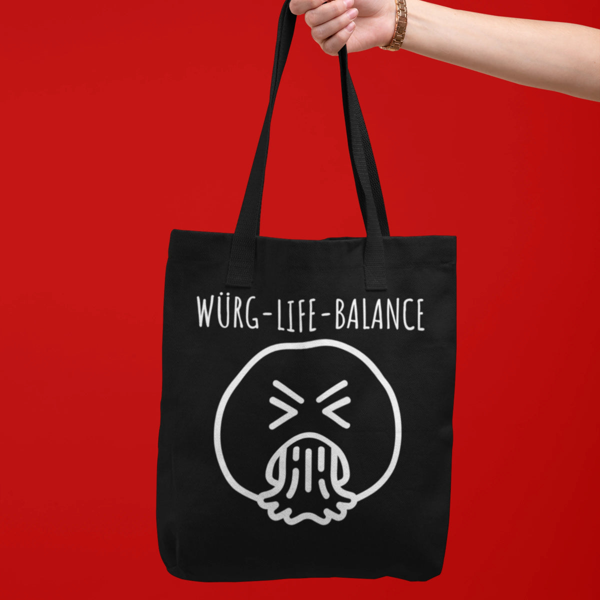 Schwarze Tragetasche mit Spruch "Würg-Life-Balance" und würgendem Smiley-Print von Vollzeitfrust, gehalten vor rotem Hintergrund